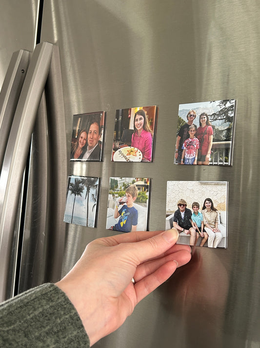 Hand placing a photo magnet on a refrigerator with other magnets.