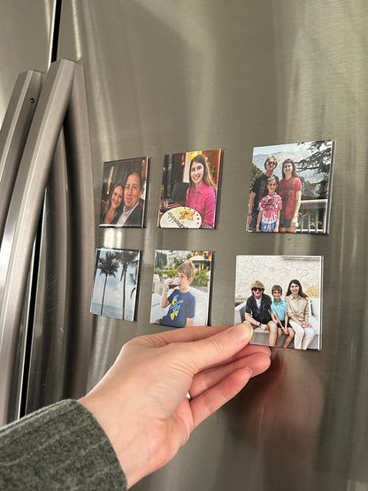 Hand placing a photo magnet on a refrigerator with other magnets.